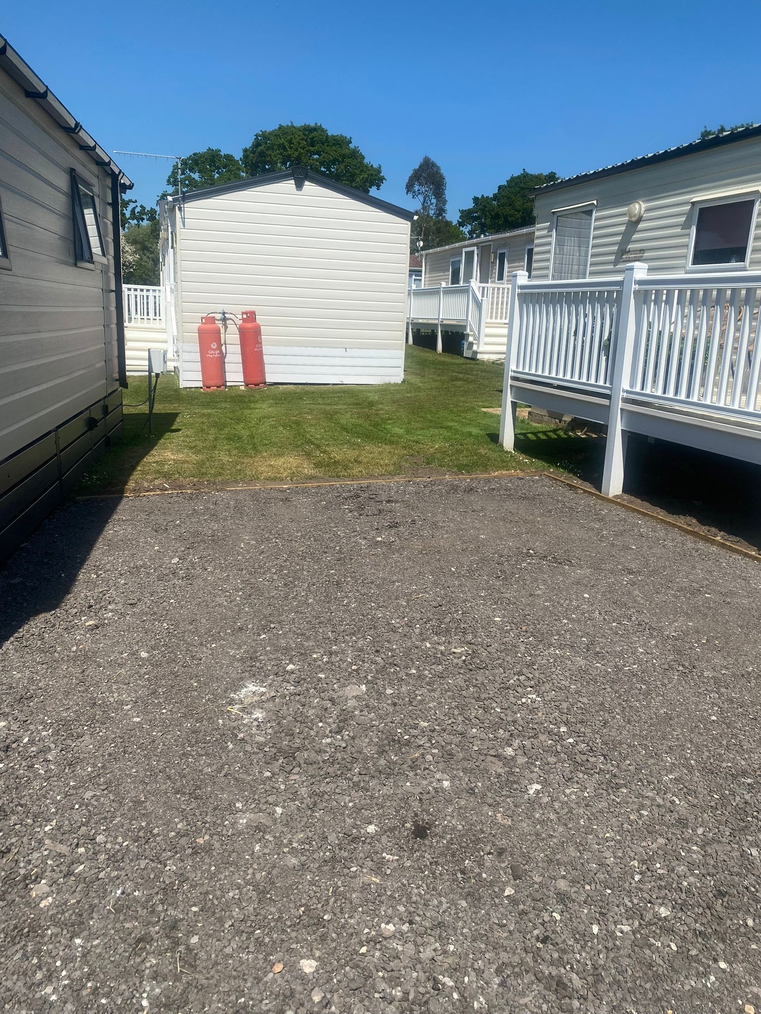 Gravel driveway in front of static caravans on a sunny day; red propane tanks on the grass.