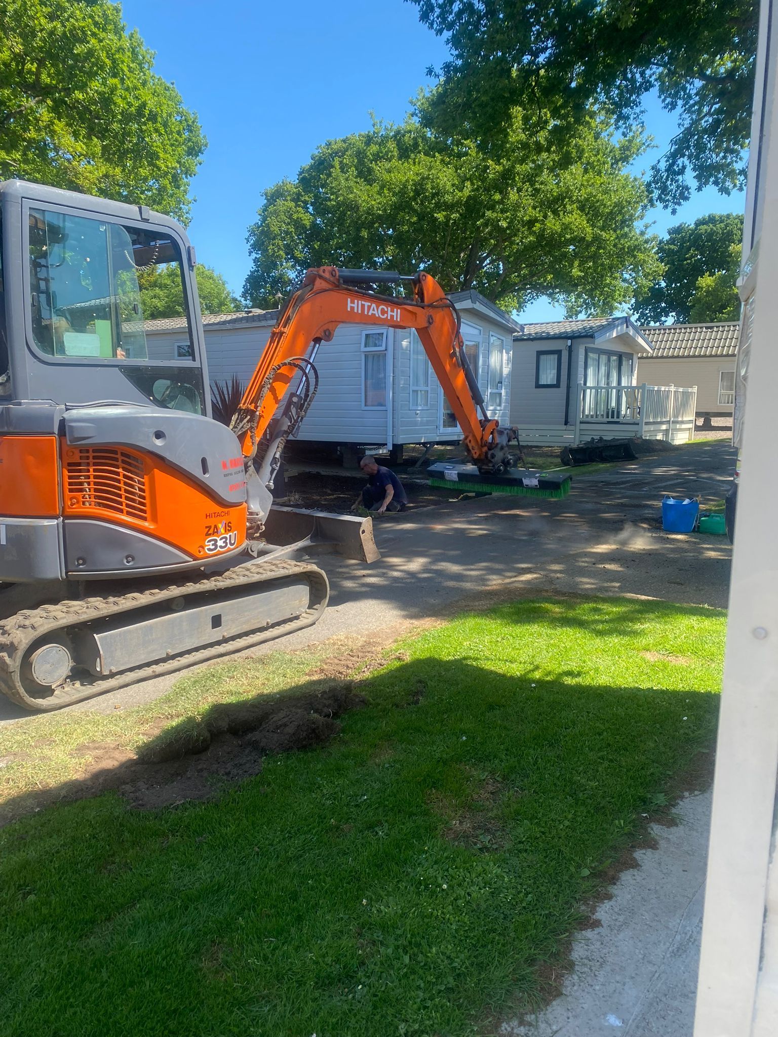 An orange excavator dismantles a mobile home on a grassy lot. Bright sunny day.