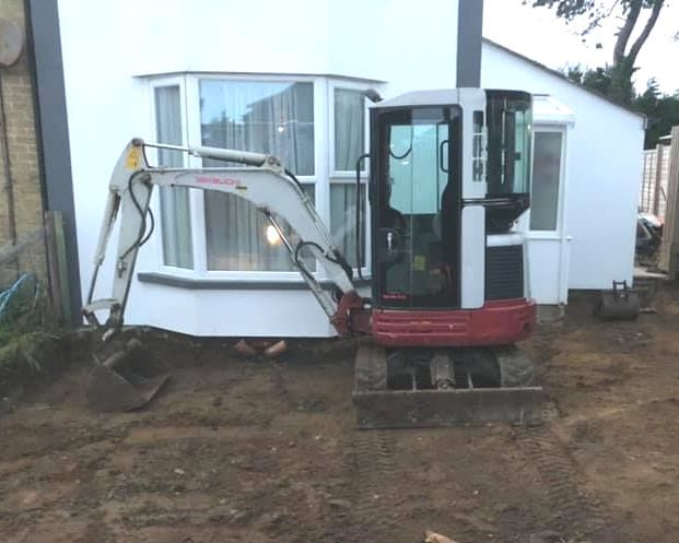 A small excavator is parked in front of a white house.