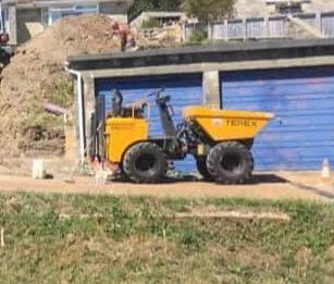 A yellow dump truck is parked in front of a garage.
