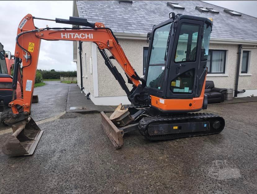 A hitachi excavator is parked in front of a house.