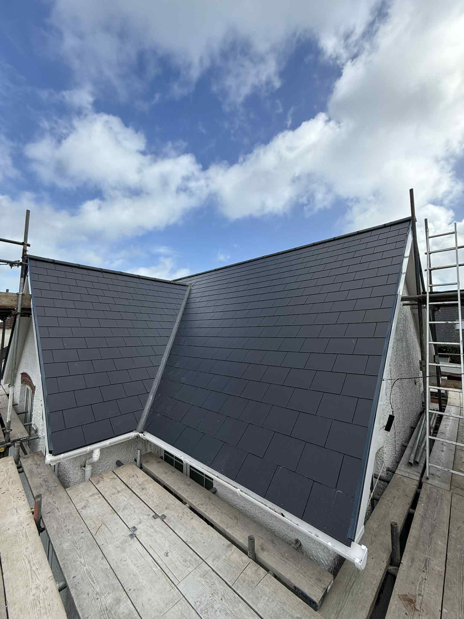 Black roof with scaffolding against a partly cloudy sky.