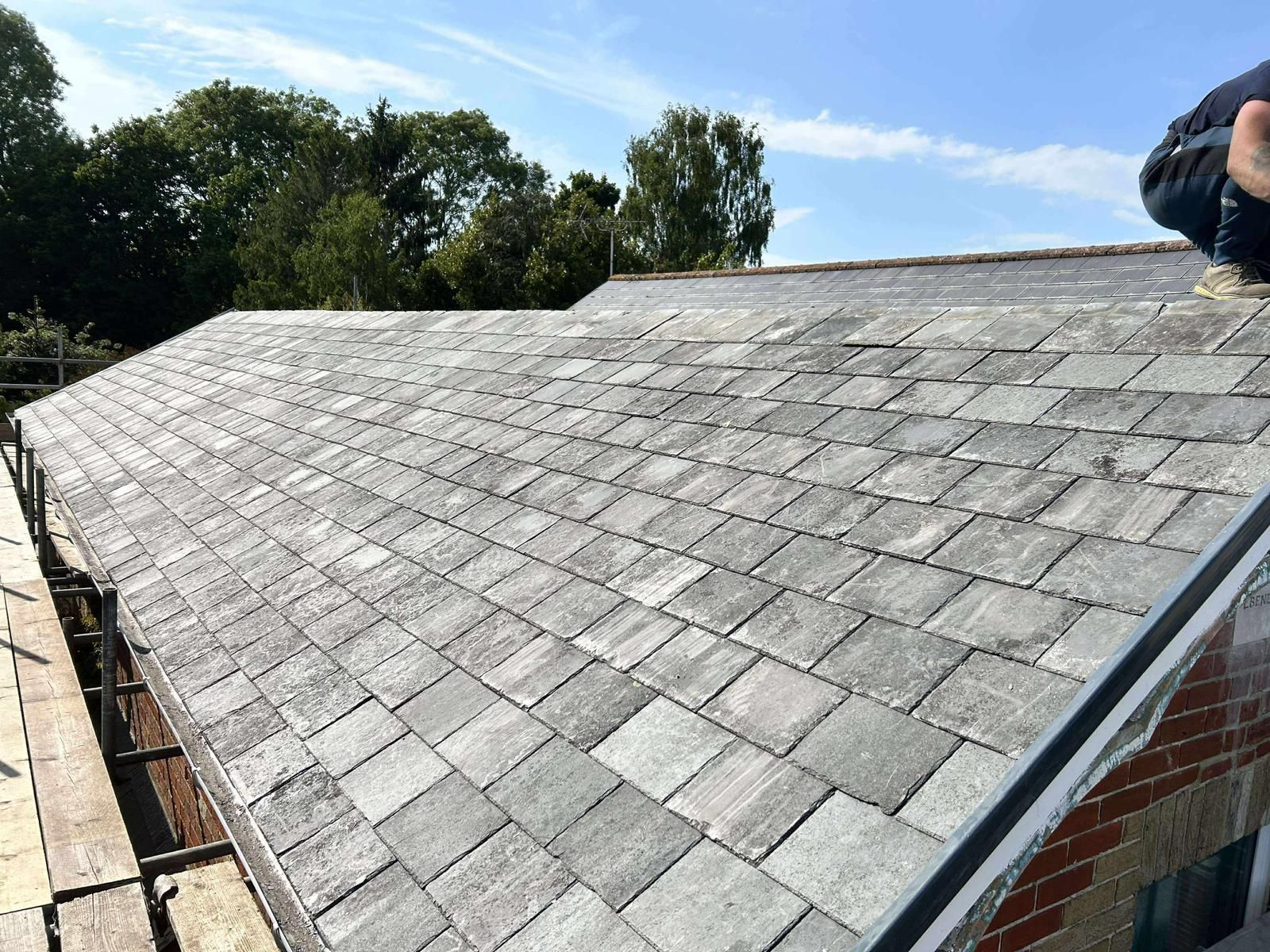 Slate roof with a worker near the top, blue sky, trees in the background.