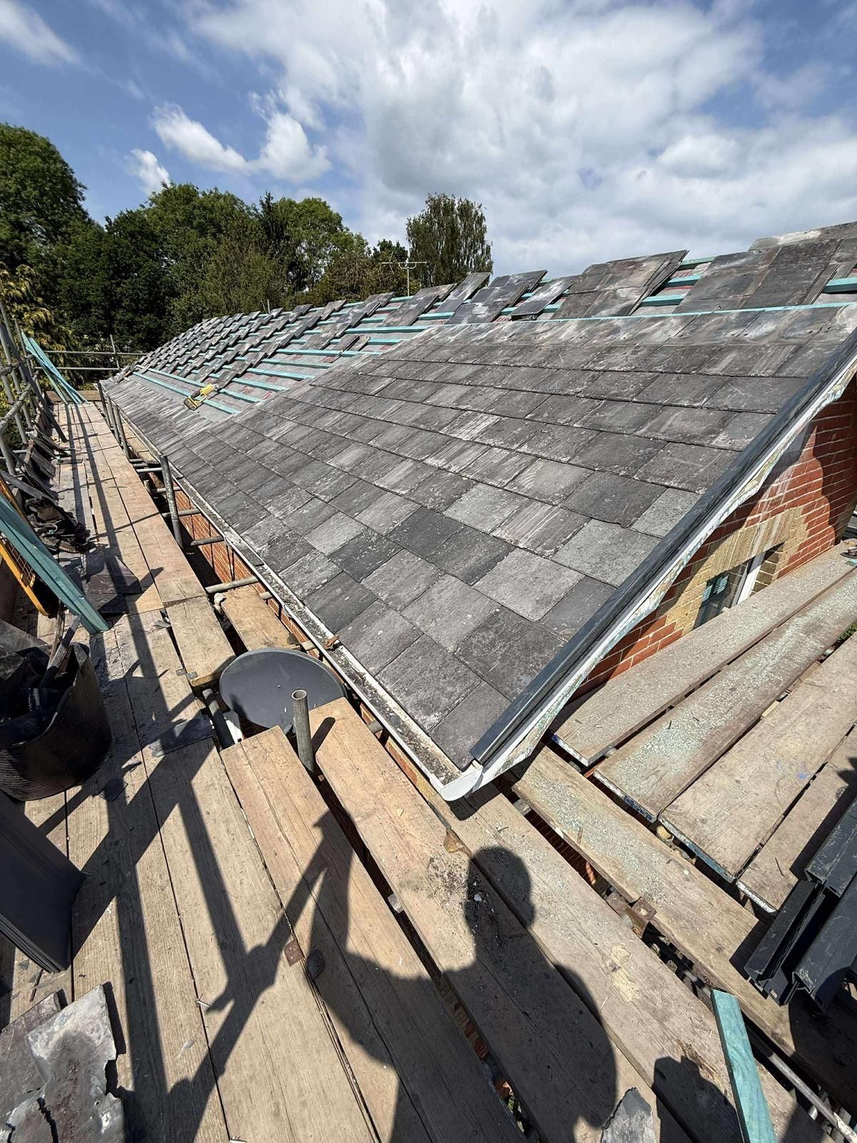 Roof partially covered in grey shingles, scaffolding, and a blue sky with clouds.