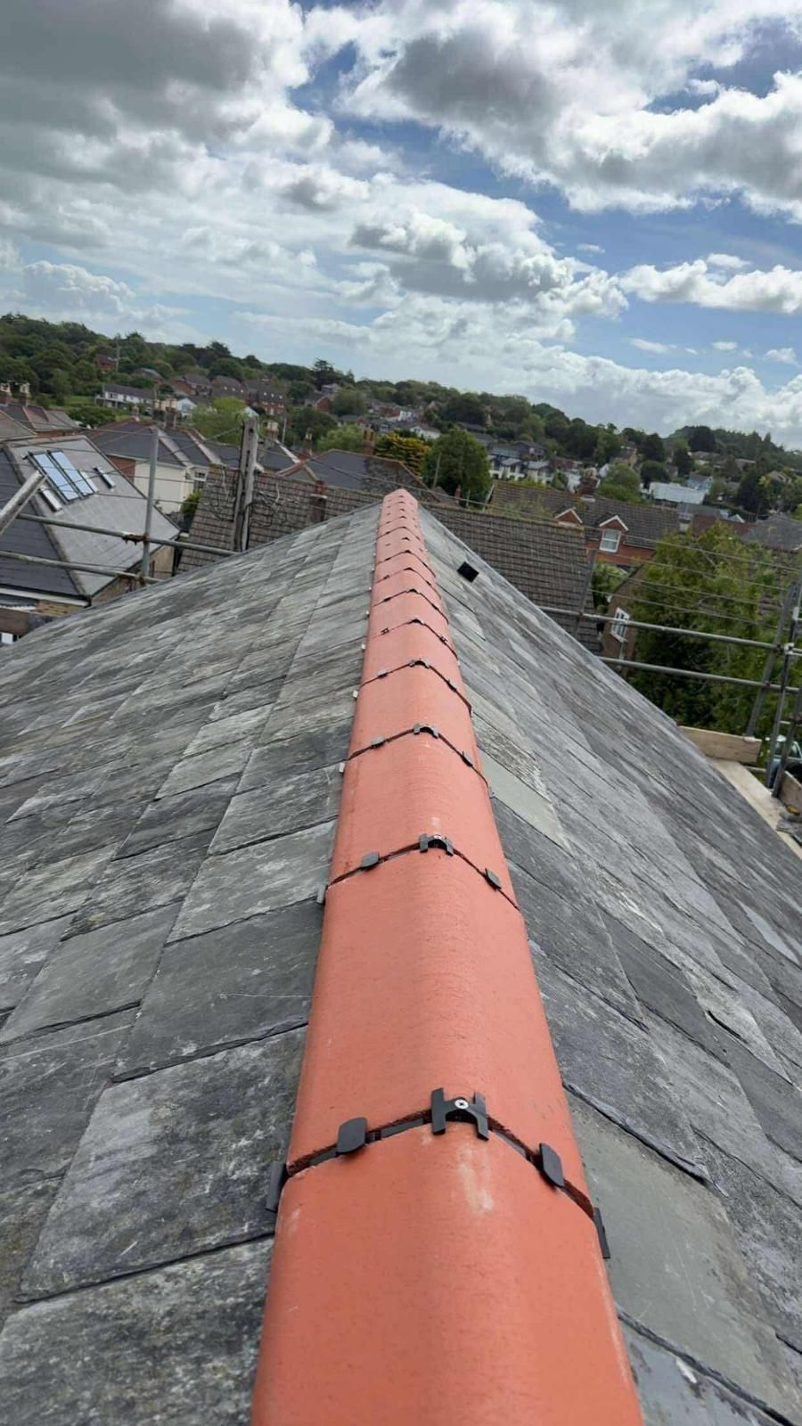 View of a tiled roof with red ridge tiles, leading to a cloudy sky.