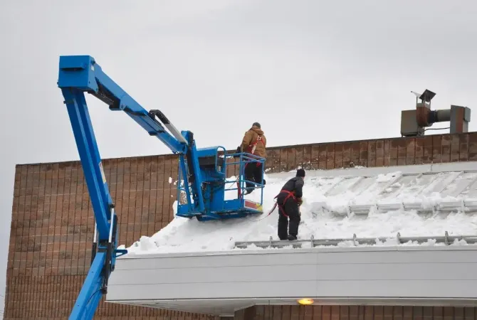Workers removing snow from a commercial roof.