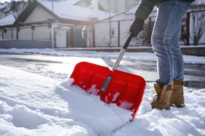 Person using a red shovel to clear snow.