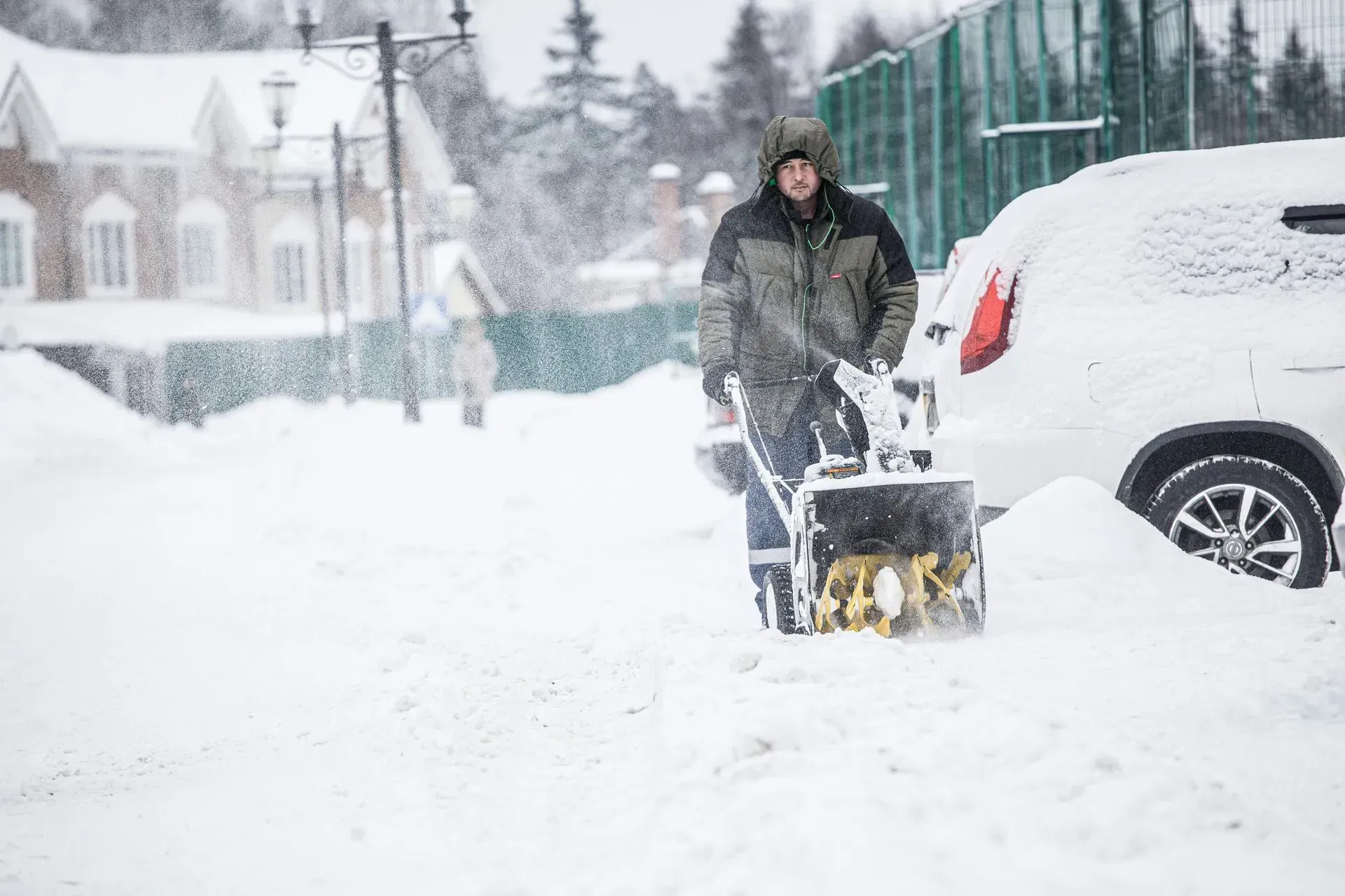 Man using a snow blower in a snowy neighborhood.