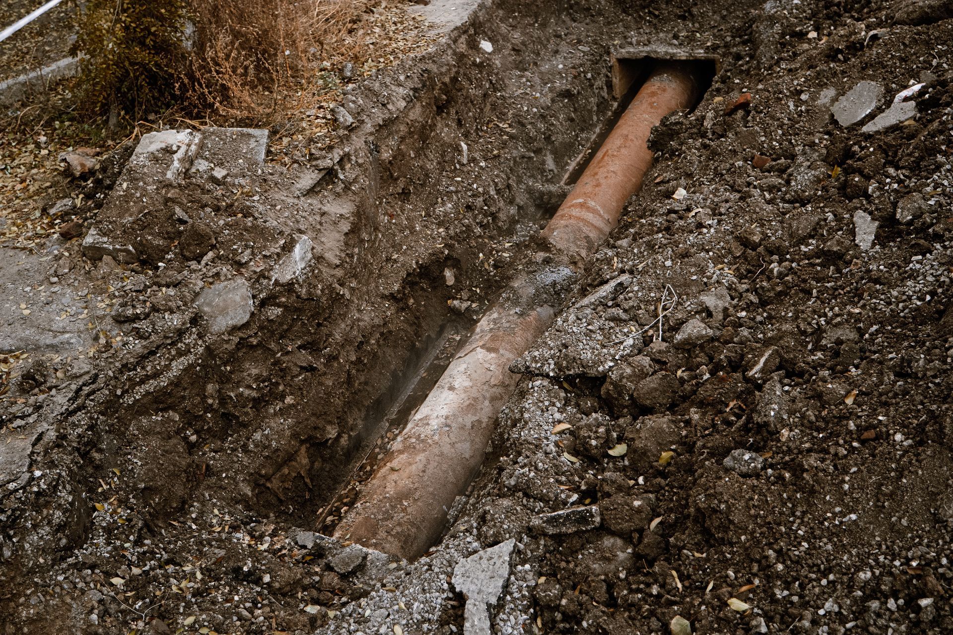 A section of an old rusty pipe exposed in a dirt trench, possibly for repair.