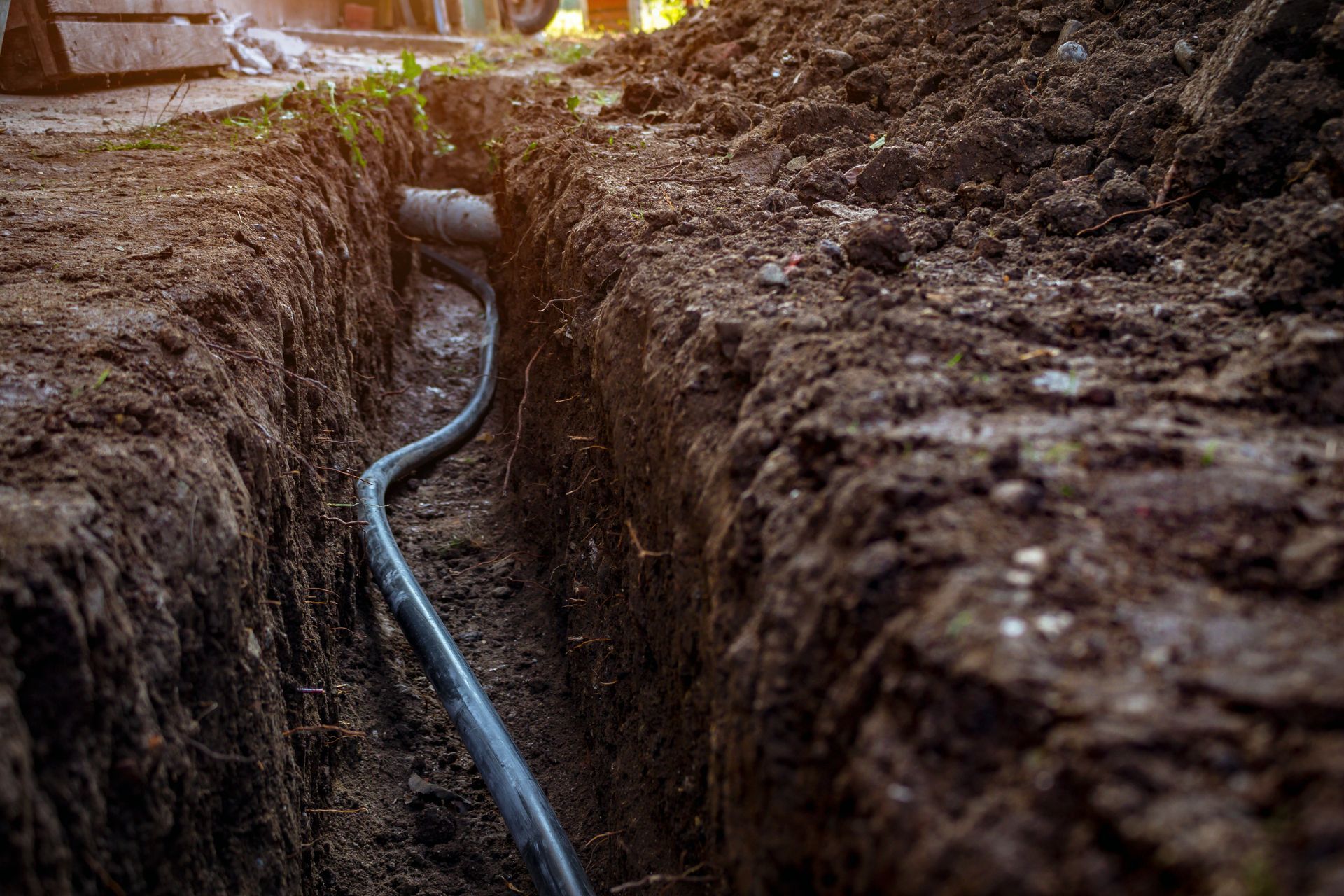 A black cable winding through a narrow trench dug in dark brown soil, outdoors.