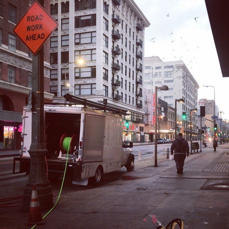 A road work truck parked on a city street; a person walks on the sidewalk.