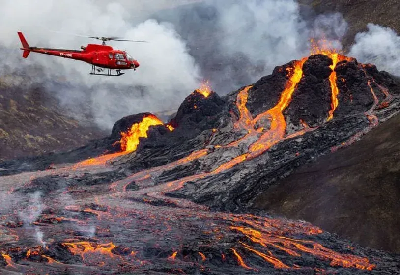 Et rødt helikopter flyr over en vulkan med lava som kommer ut av den.