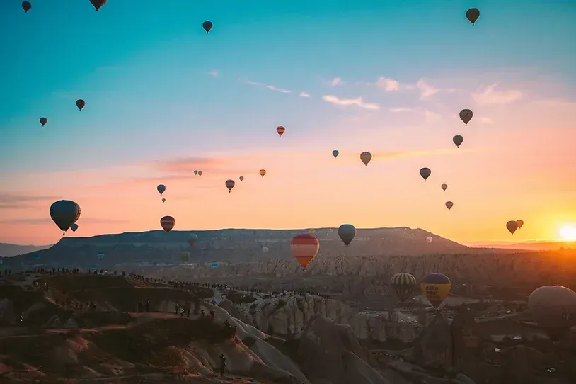 En haug med luftballonger flyr på himmelen ved solnedgang.