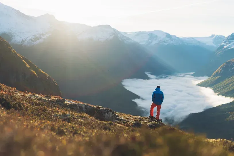 En mann står på toppen av et fjell med utsikt over en dal.