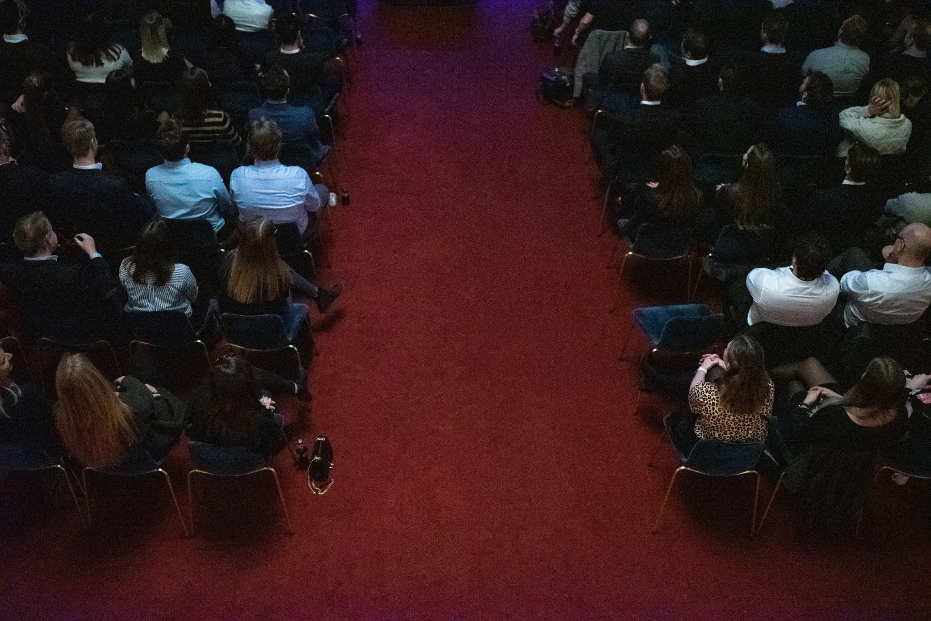 En stor gruppe mennesker sitter i et mørkt auditorium.