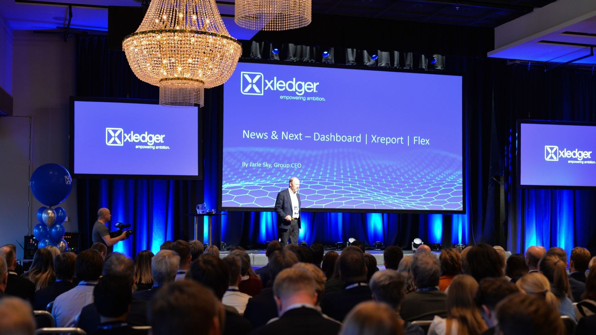 En mann holder en presentasjon foran en stor skjerm som sier xledger