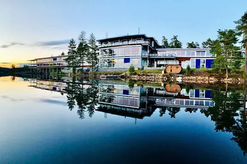 En stor bygning reflekteres i vannet i en innsjø.