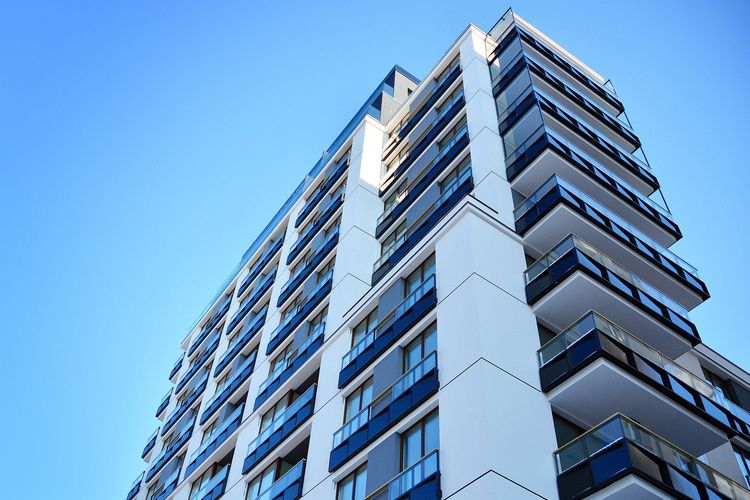 Low-angle view of a modern white apartment building against a clear blue sky