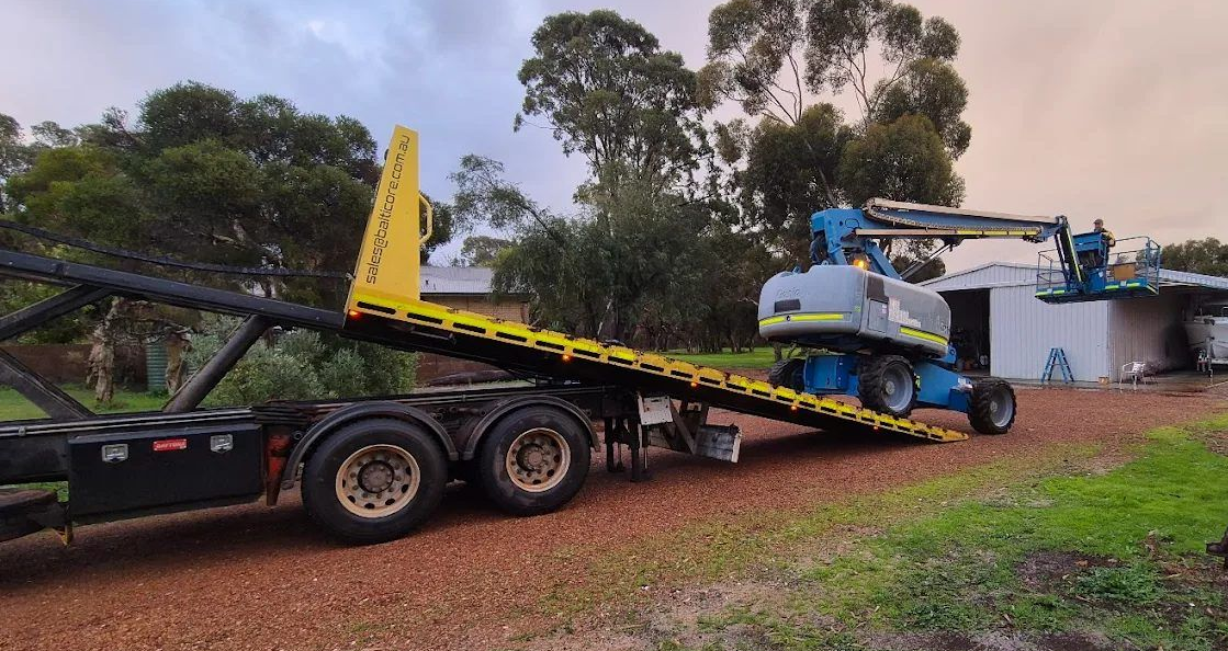 Balticore tilt tray with the deck down while a boom lift drives on at a shed
