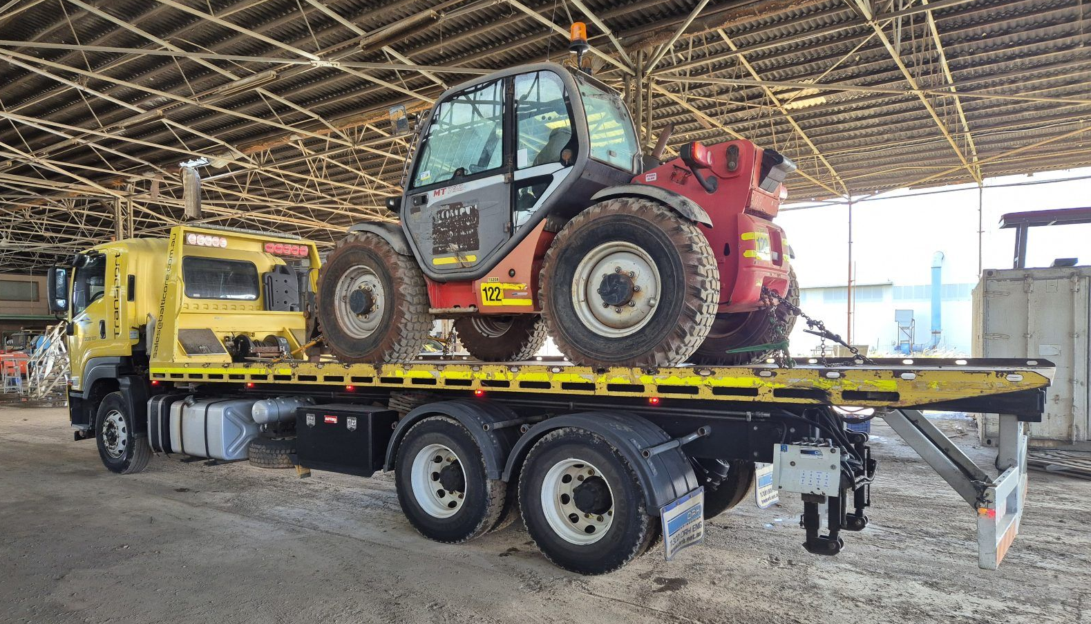 Balticore tilt tray truck with a telehandler chained on inside a warehouse