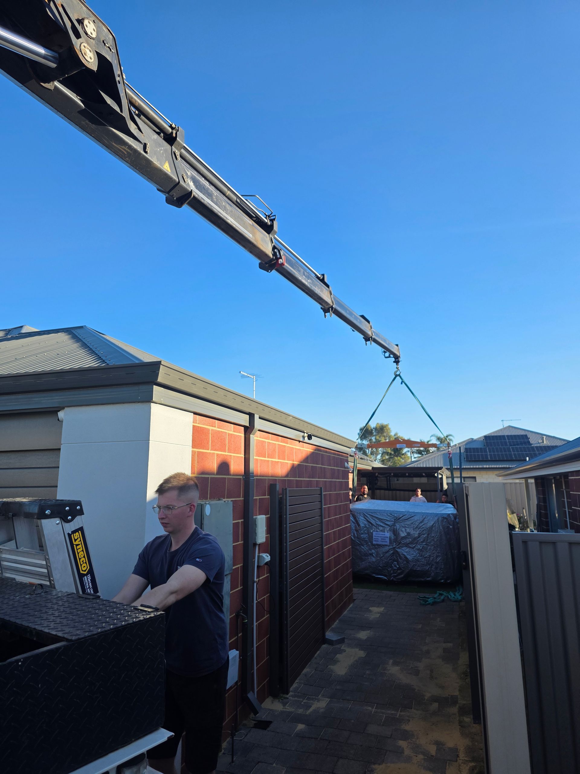 Hiab crane arm reaching over a Perth roof to place a spa