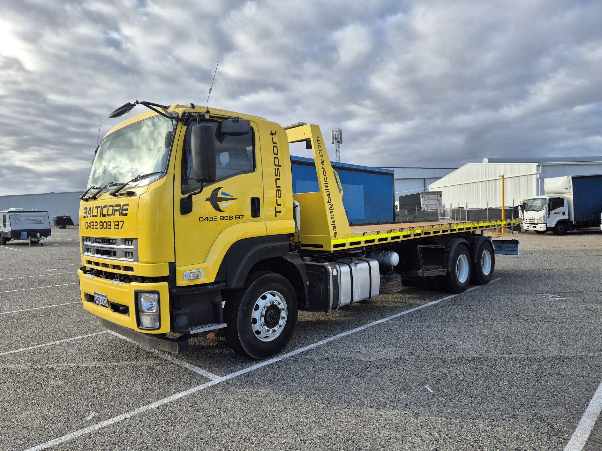 Yellow tow truck on a paved lot; blue sky with clouds in the background.