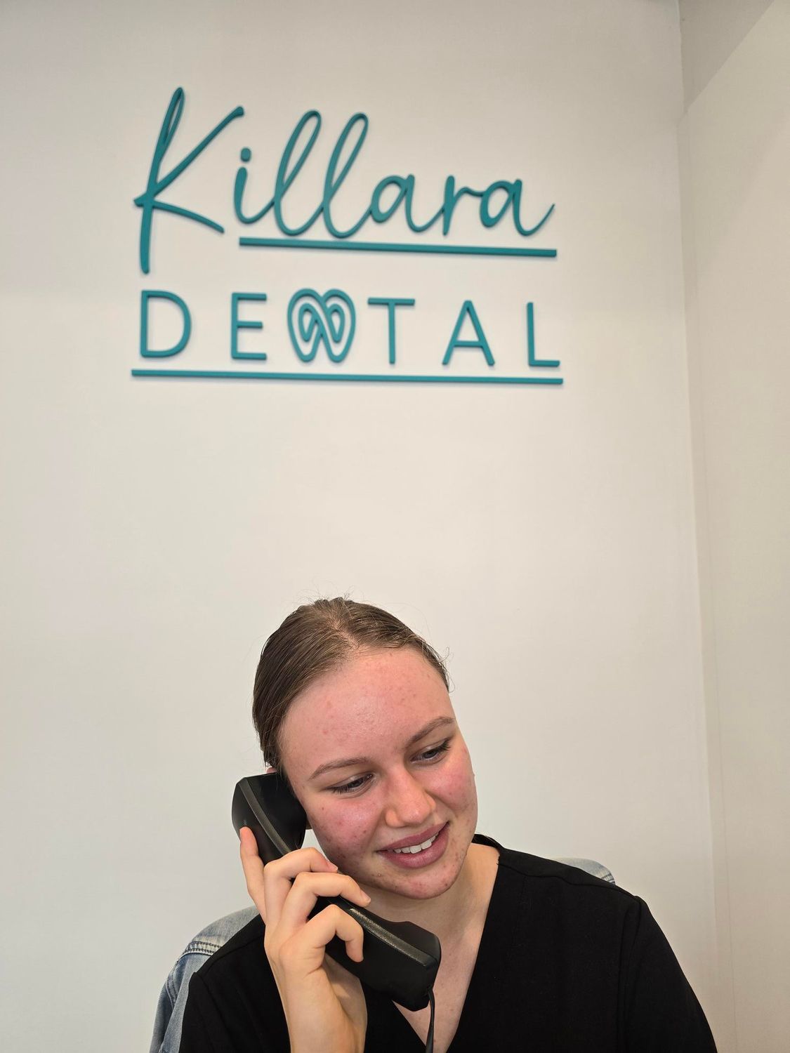 Woman smiling on the phone beneath a Killara Dental sign — Killara Dental in East Killara, NSW