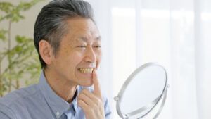 A Person Looking Into a Handheld Mirror and Pointing at Their Teeth — Killara Dental in East Killara, NSW