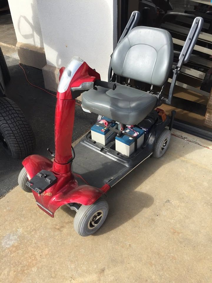 Red mobility scooter parked outdoors beside a wall, with a black seat and front basket.