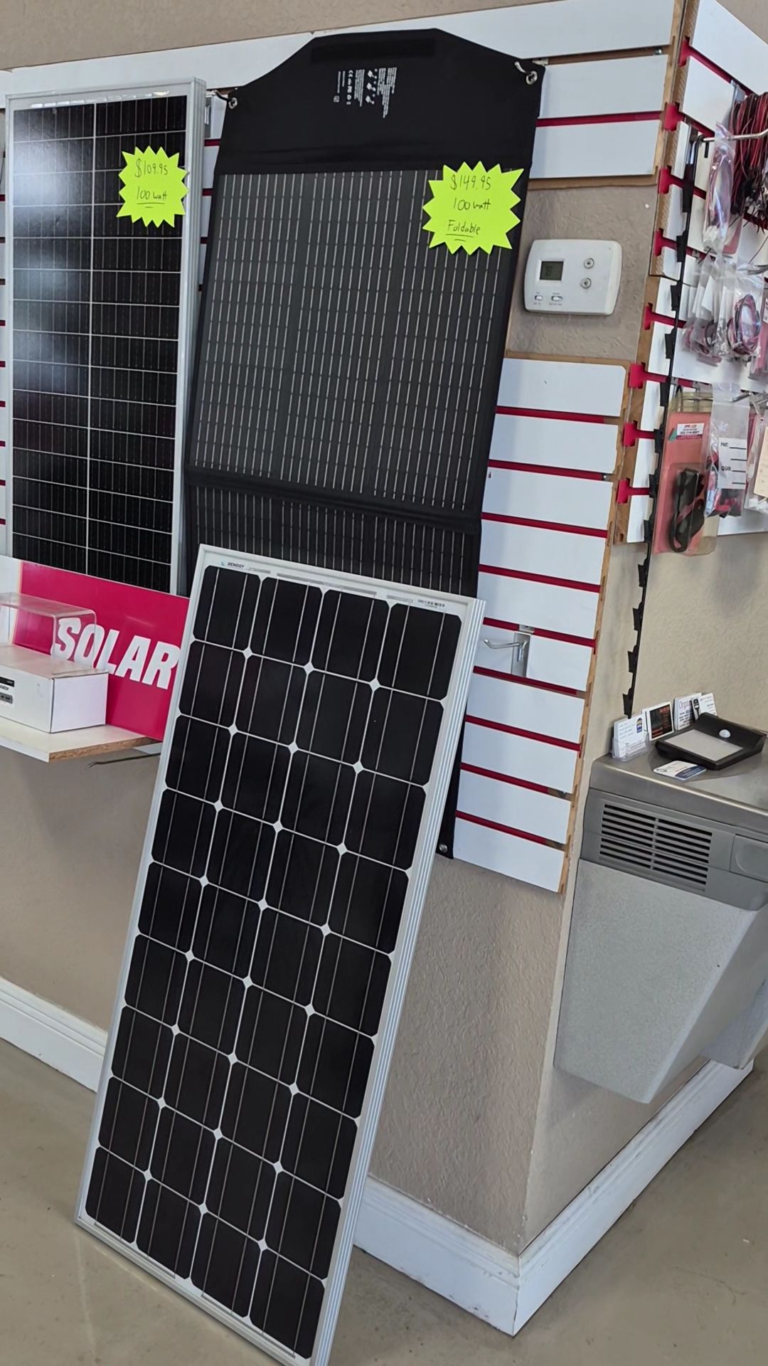 Solar panel display leaning against a wall in a store, with a black solar charger above it.