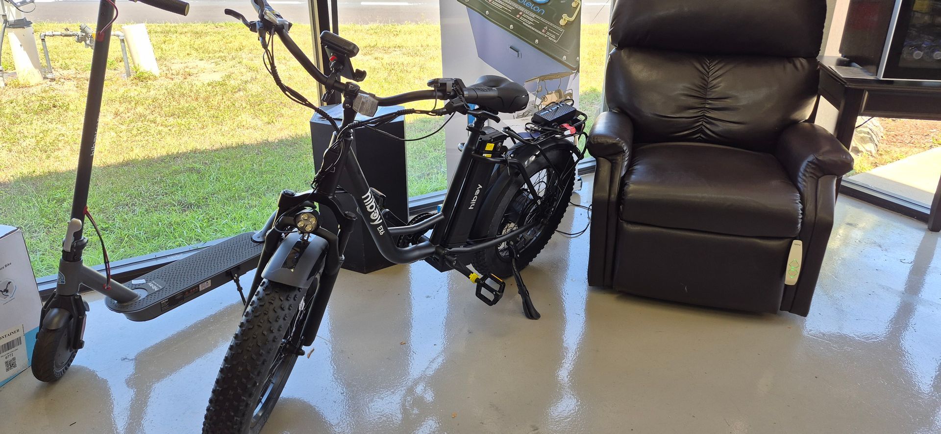 Black electric bike indoors by a leather recliner on a screened porch, with a scooter nearby
