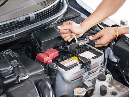 Hands using a wrench to tighten a car battery in an engine bay.