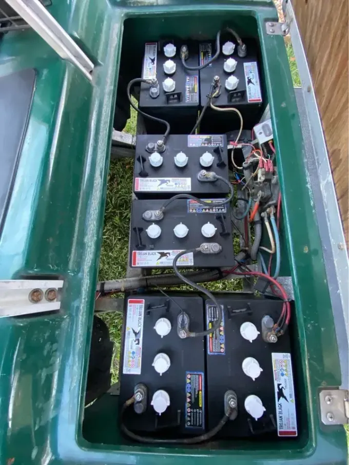 Open battery compartment with several wired black batteries and electrical components inside a green vehicle.