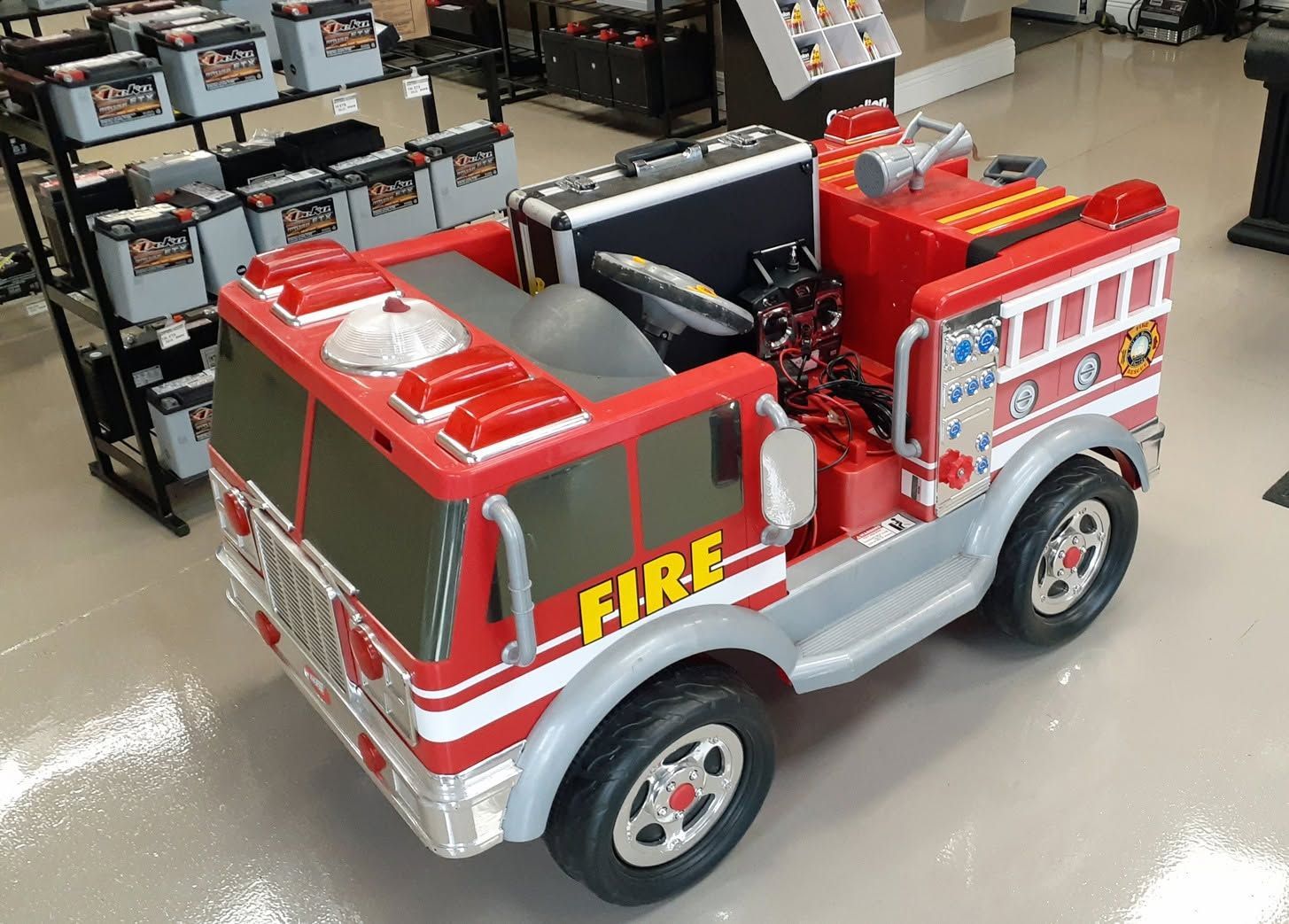 Toy red and silver fire truck on a store floor, with black seats and “FIRE” on the side