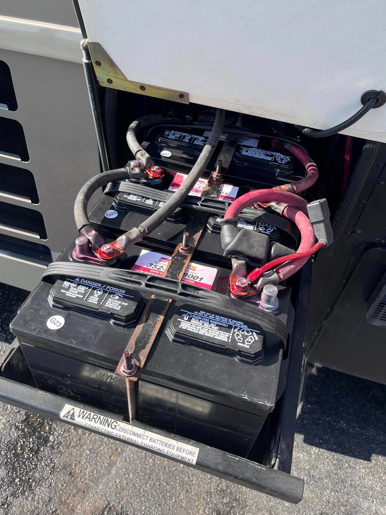 Two black batteries with red and black cables inside an open equipment compartment.