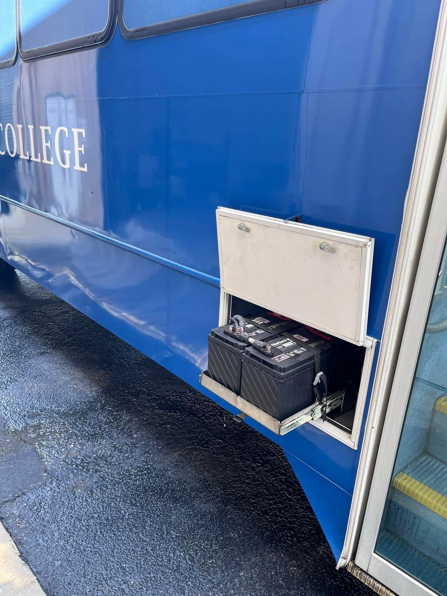Blue college building wall with an open hatch revealing a crate inside, next to a glass door on a wet sidewalk.