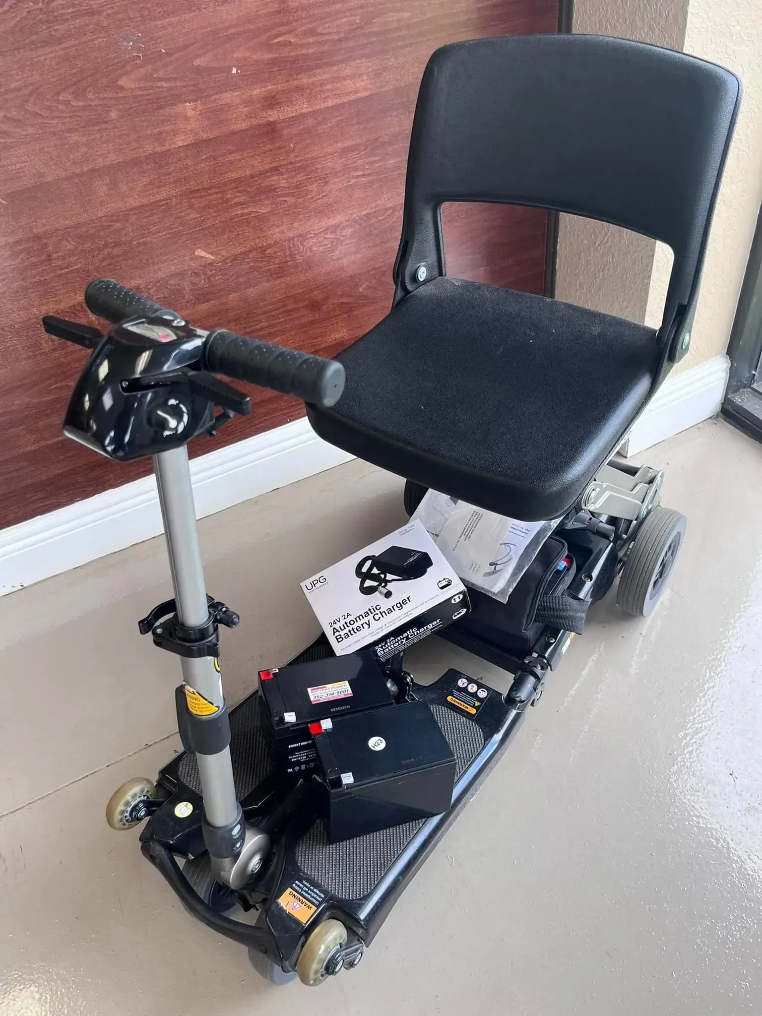 Black mobility scooter with a seat in a room with a wood wall and tiled floor