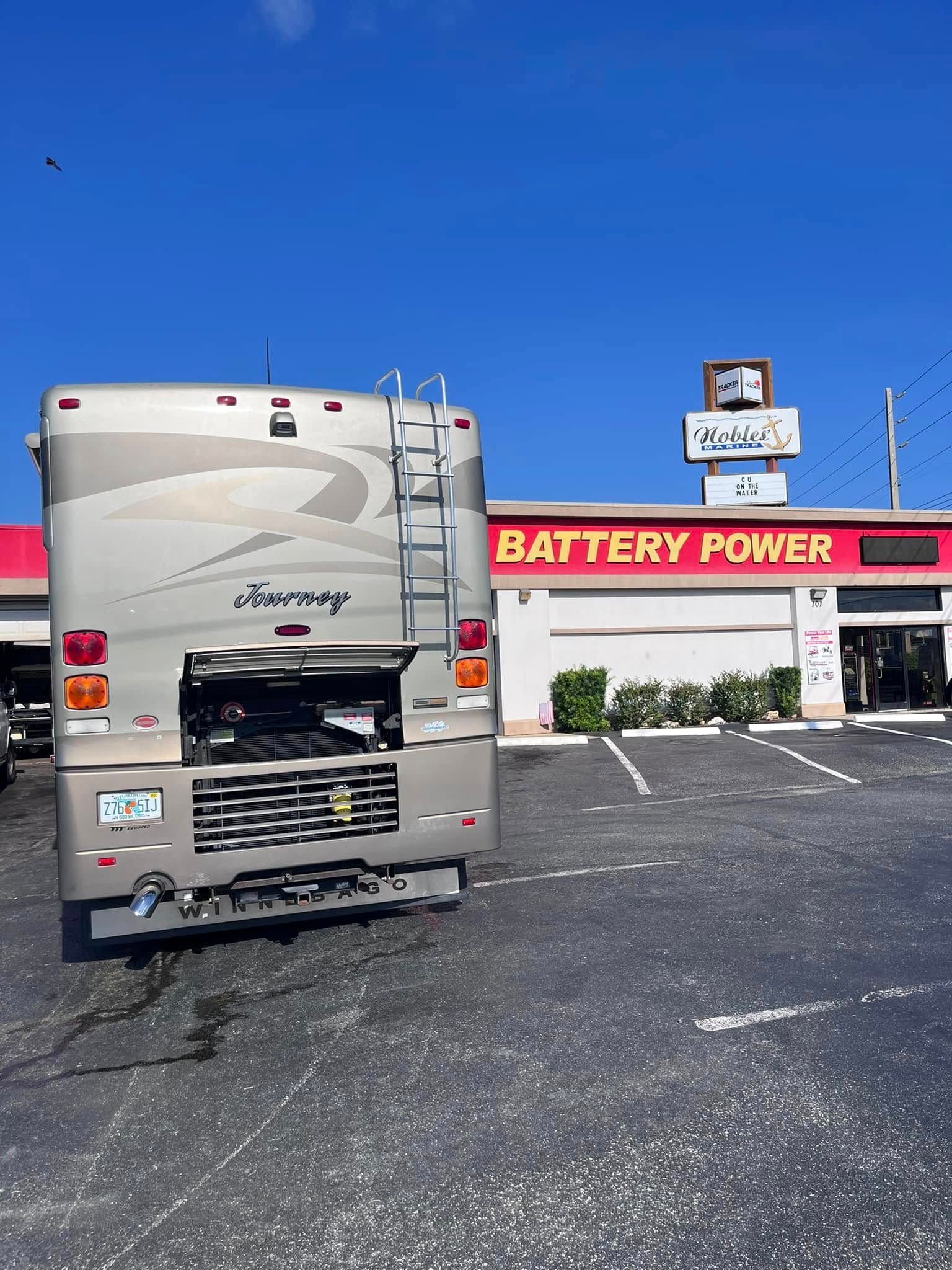 Silver RV parked outside Battery Power store under a clear blue sky.