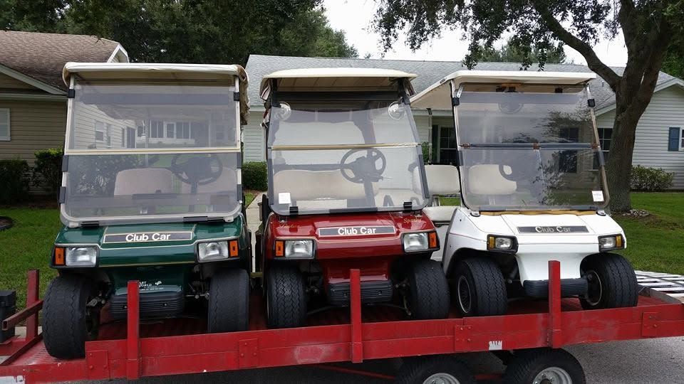 Three colorful golf carts—green, red, and white—lined up on a red trailer outdoors.