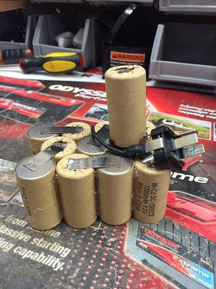 Pile of beige cylindrical batteries with black wires on a red-and-black workbench mat