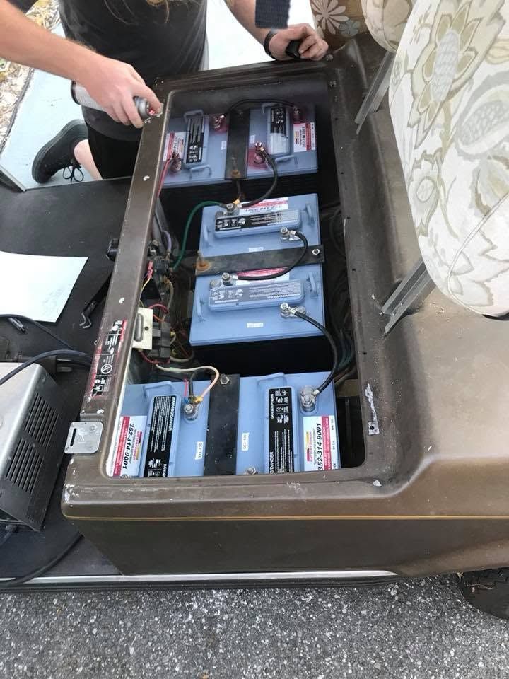 Open storage box with batteries and wiring beside a person kneeling outdoors