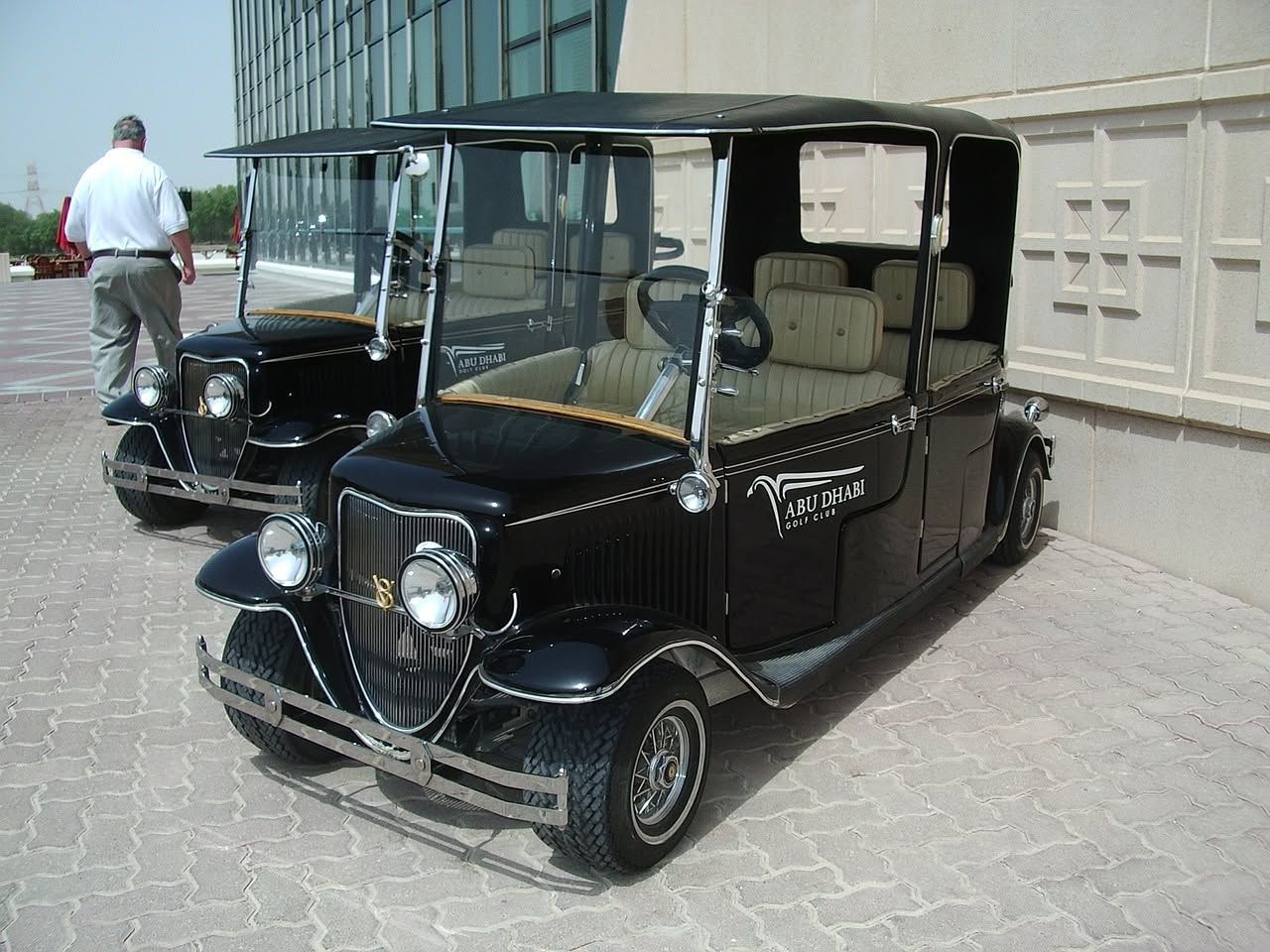 Two vintage black cars parked outside a building, one with its side door open