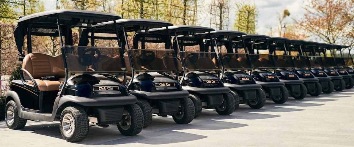 Three small golf carts in green, red, and white on a red trailer outdoors.