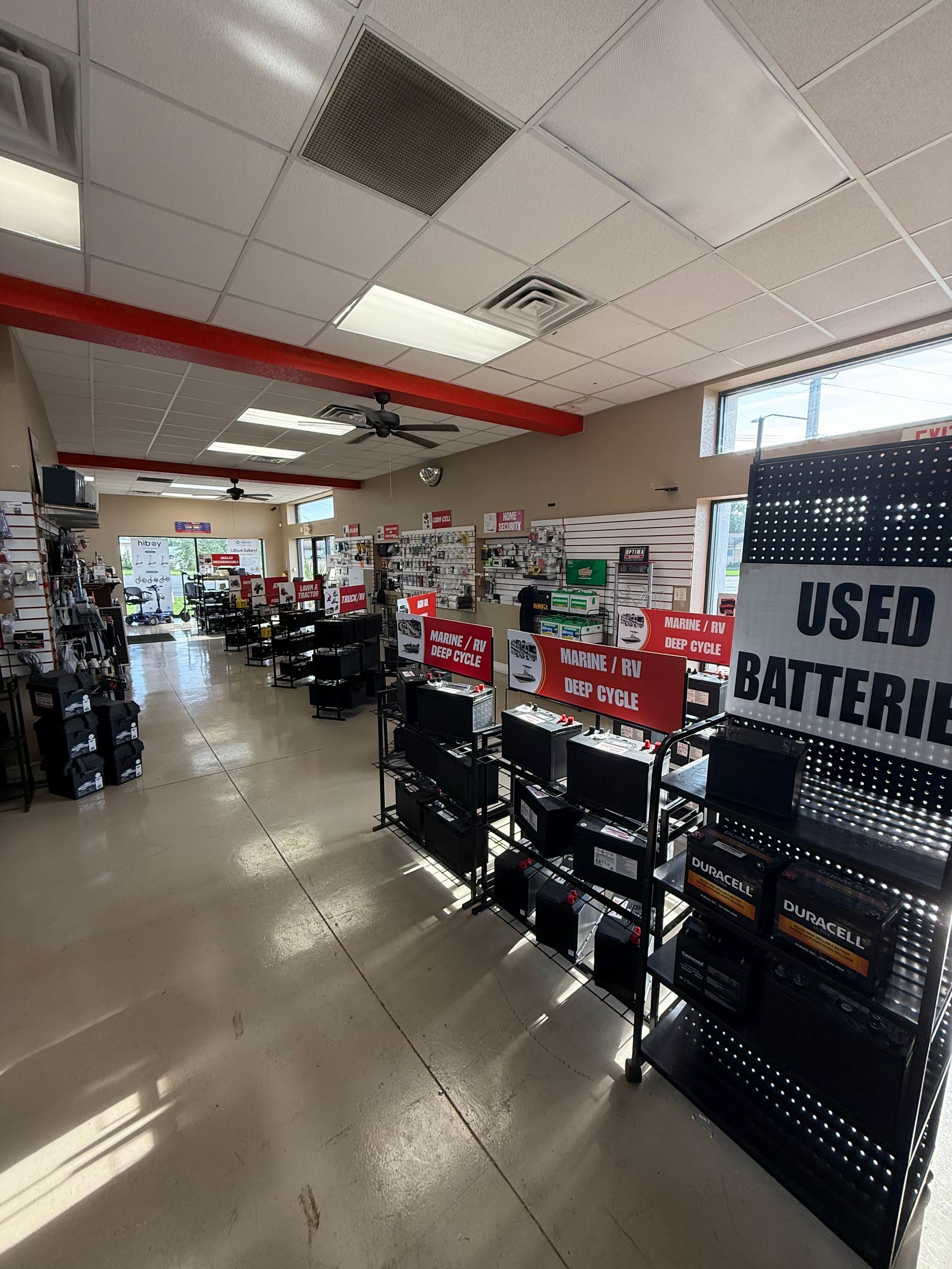 Auto parts store aisle with battery racks and a “USED BATTERIES” sign under fluorescent ceiling lights
