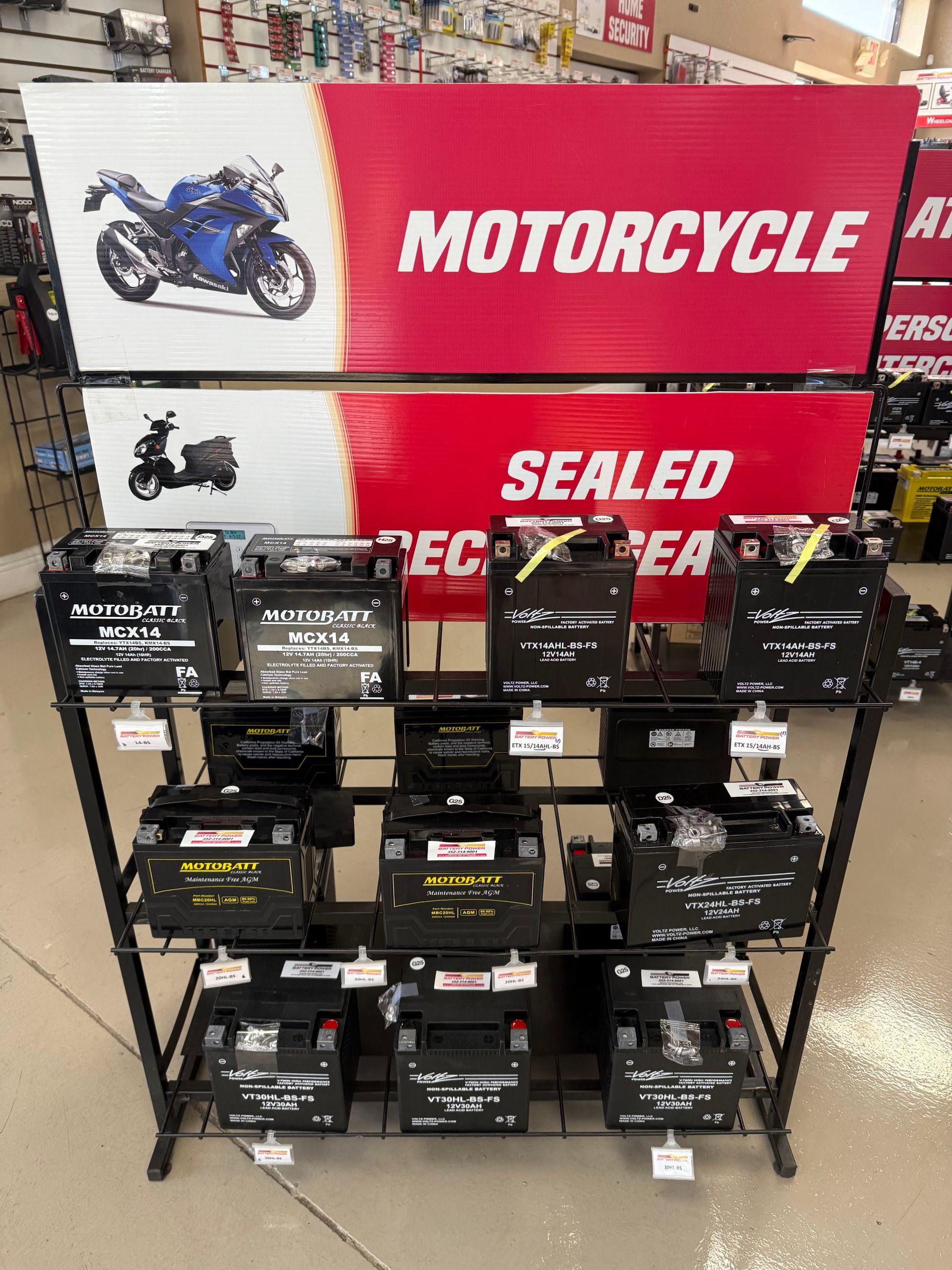 Display of sealed motorcycle batteries on a store shelf with red motorcycle signage in the background