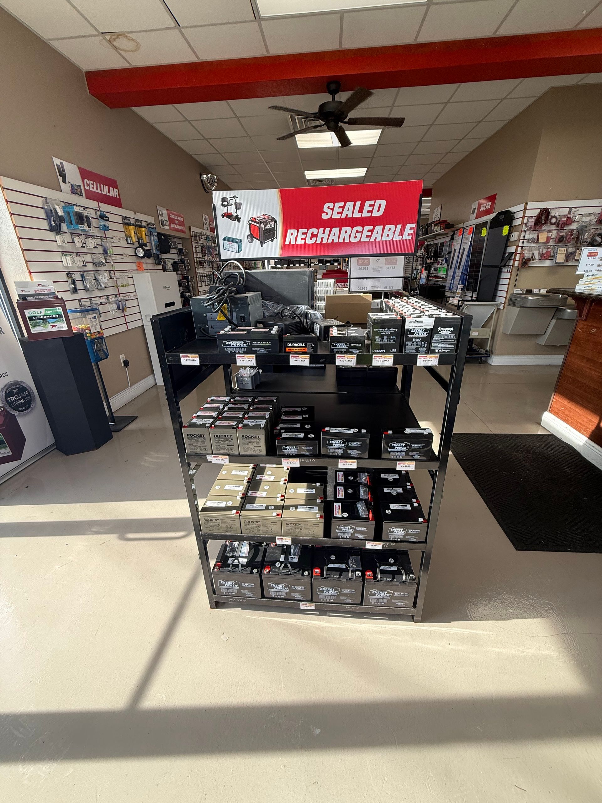 Retail store aisle with shelves of electronics accessories and a red “sale” sign overhead