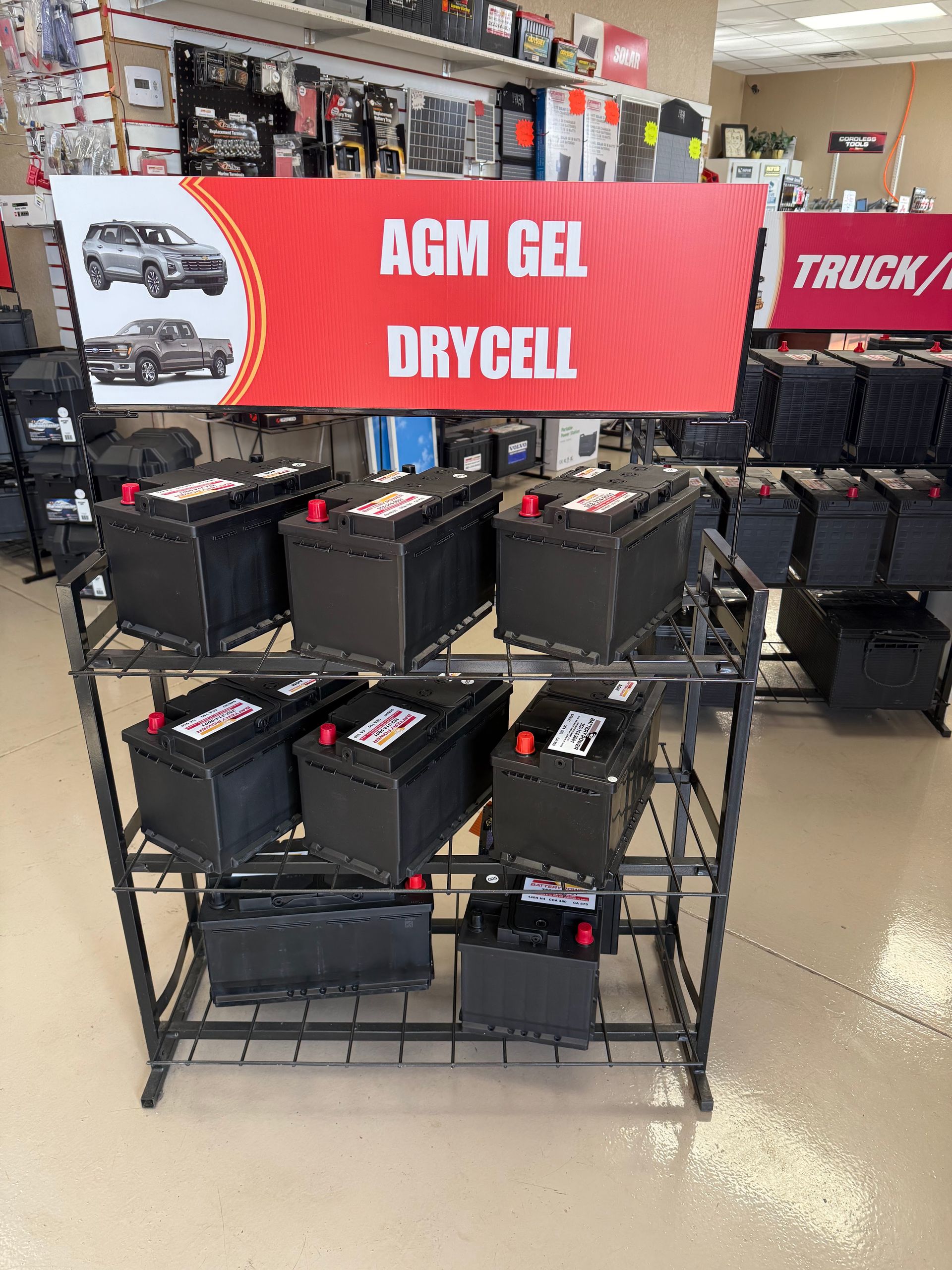 Display of AGM gel dry cell truck batteries on a store rack under a red sign.
