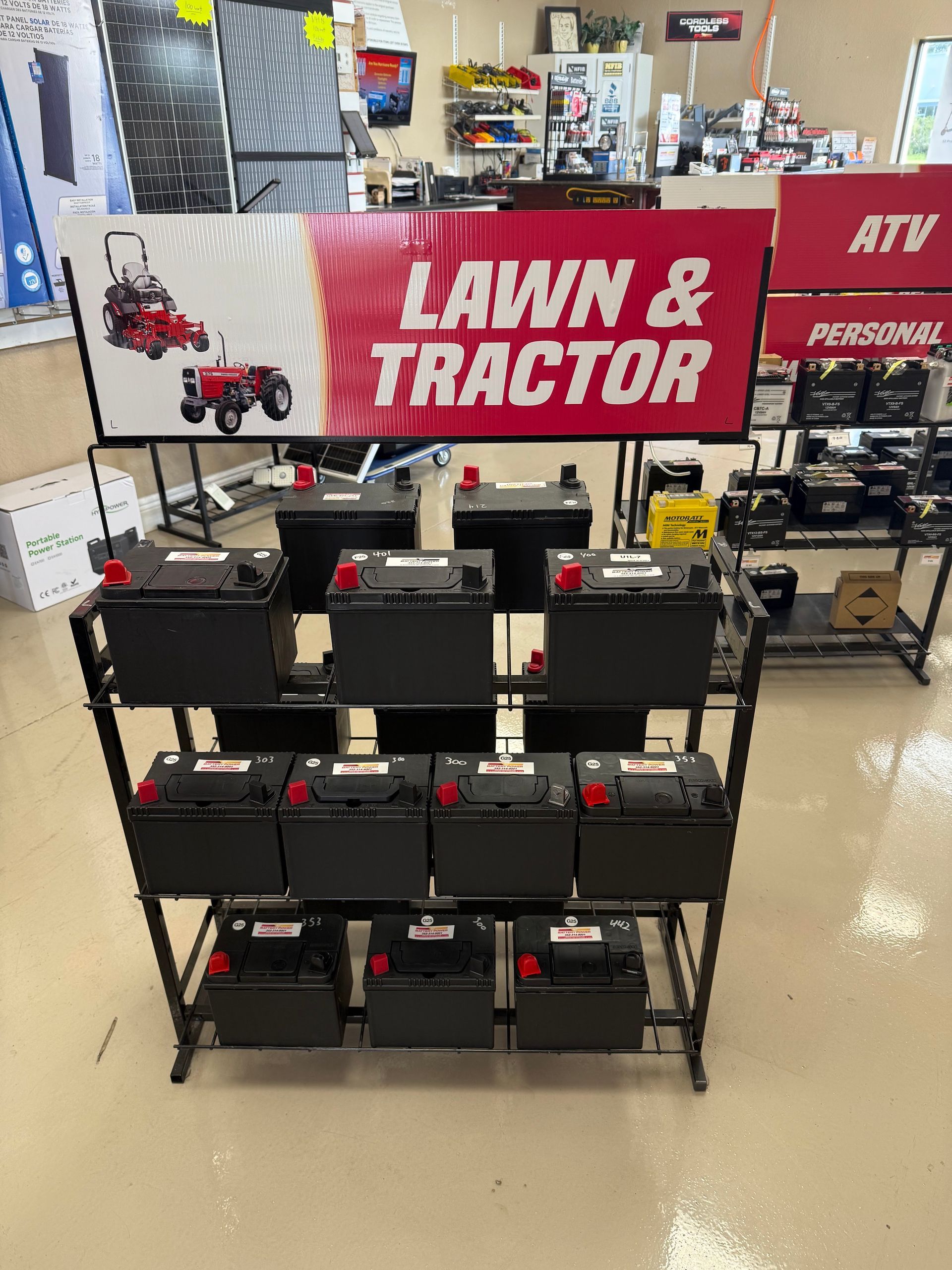 Retail store display of black batteries beneath a red “Lawn & Tractor” sign and other outdoor equipment.