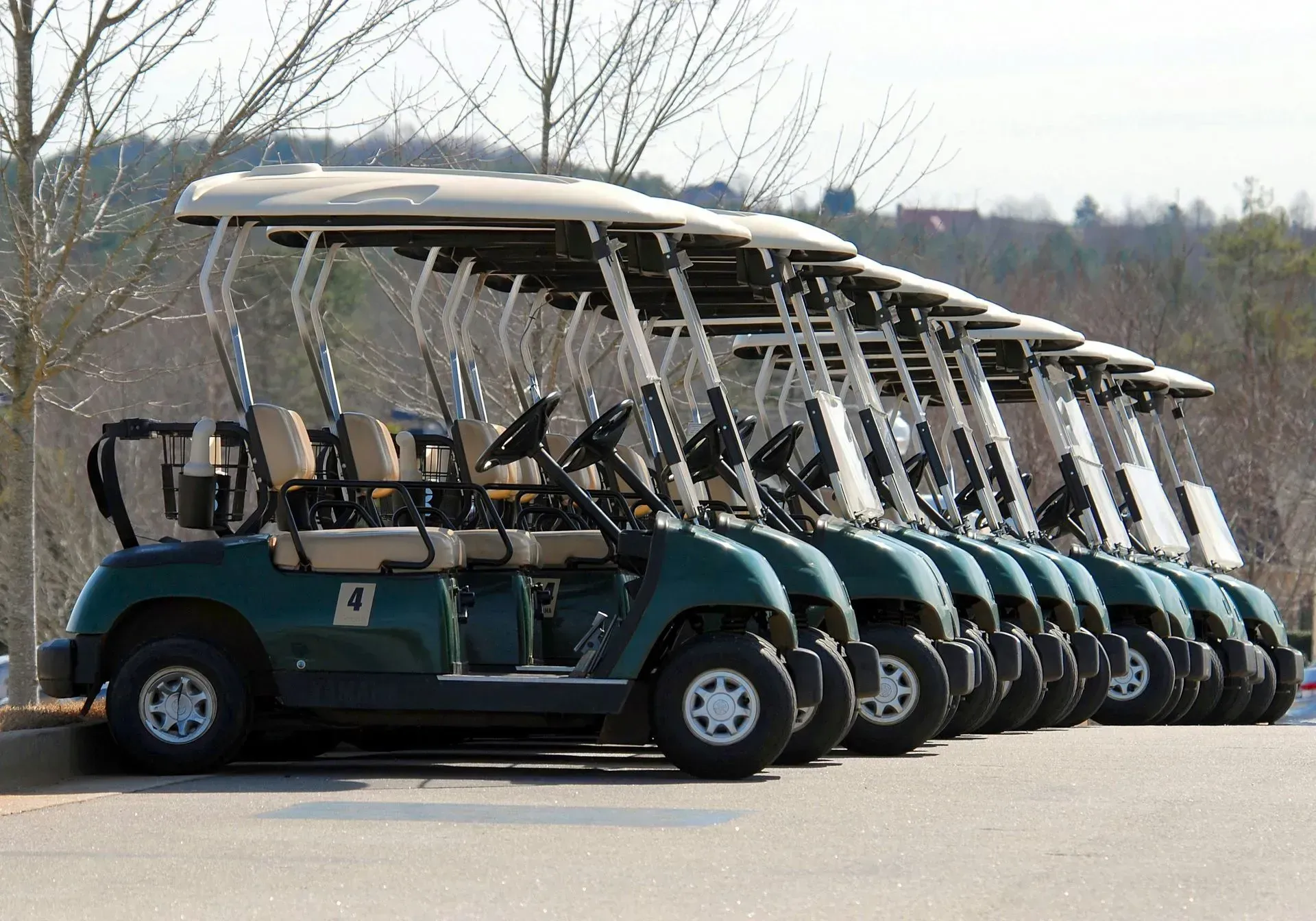 Row of green golf carts parked side by side on a lot, viewed from the front at an angle.
