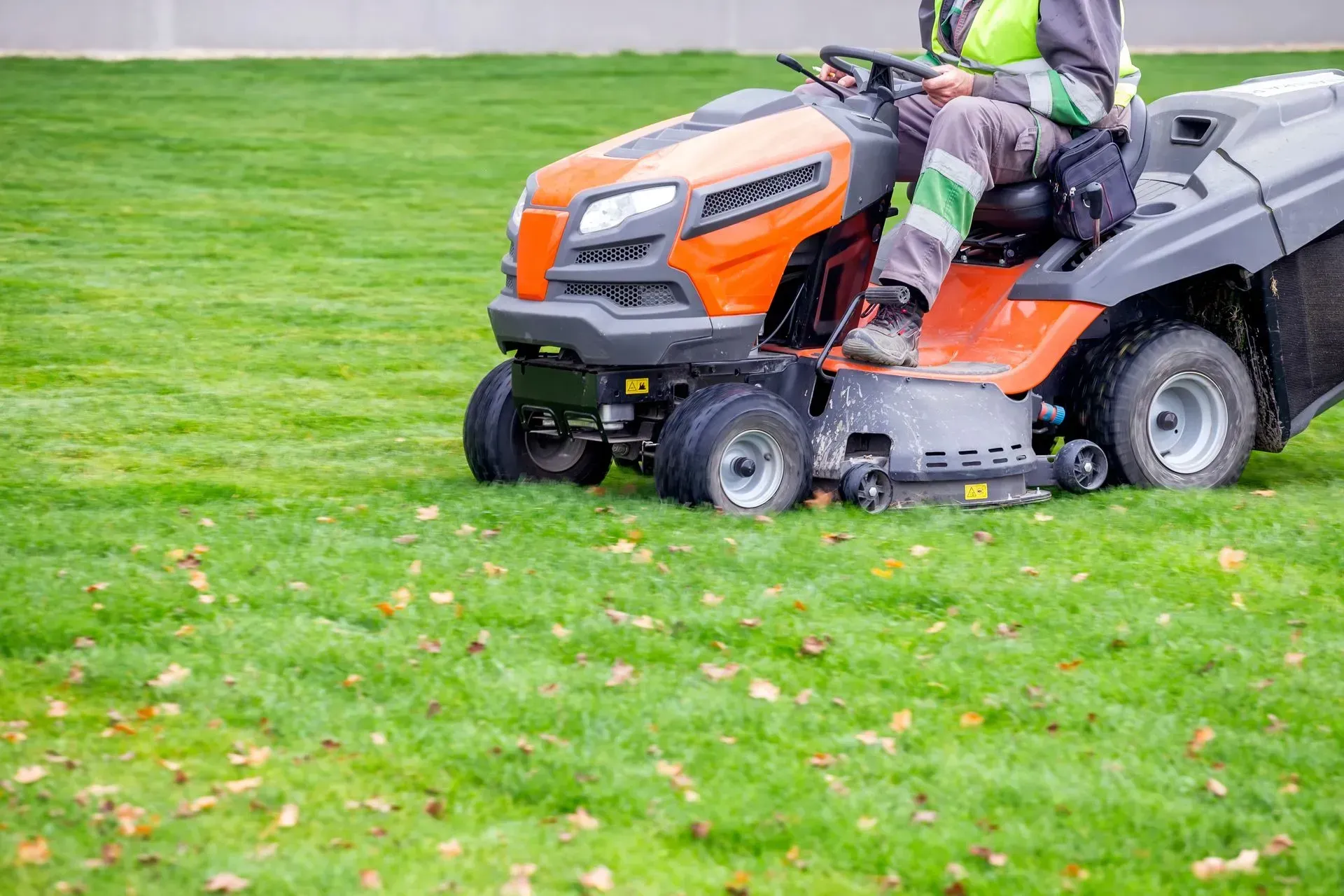 Person mowing a grassy lawn with an orange riding mower and trailer attached